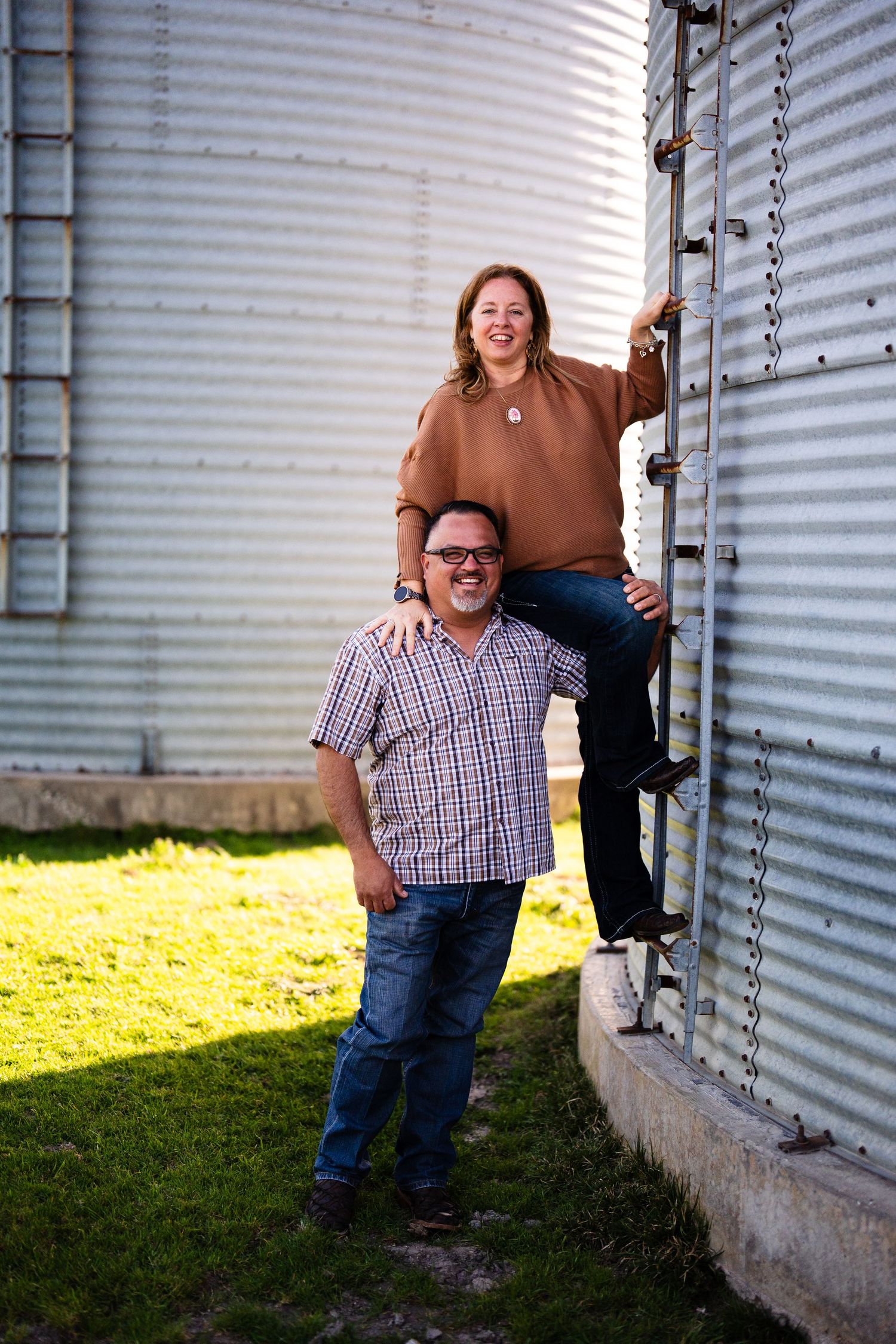 A playful outdoor portrait against a metal grain silo in warm sunlight on grassy ground.