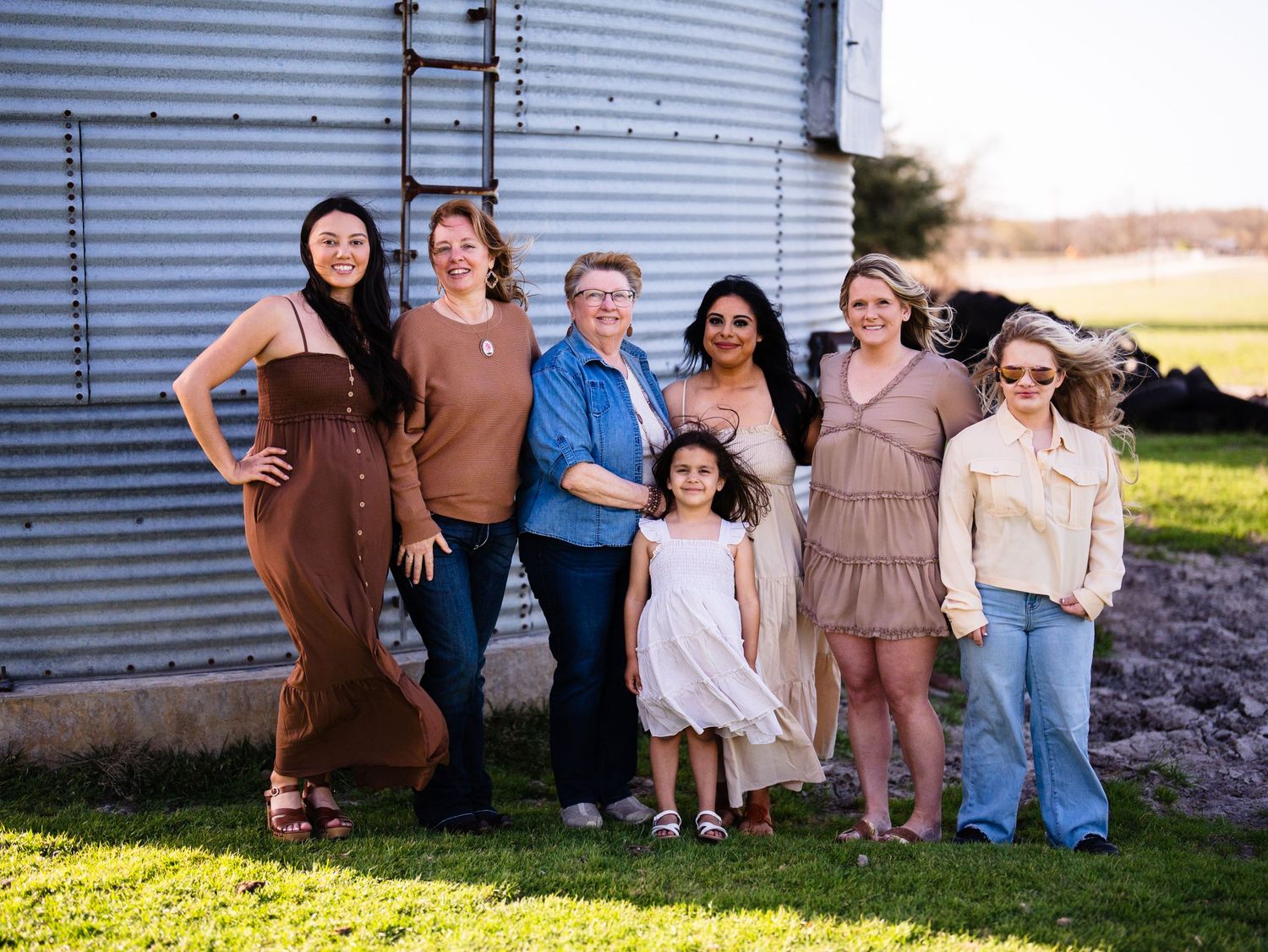 A group poses together against a silver grain silo on a sunny farm day.