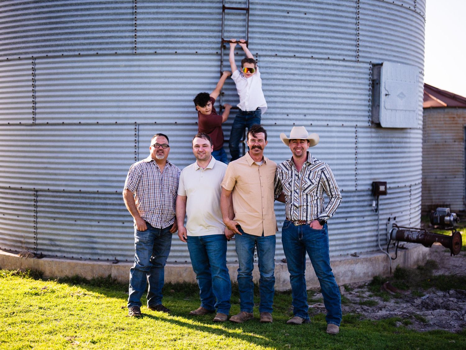 A group of people standing together outdoors next to a large metal grain silo on a sunny day.