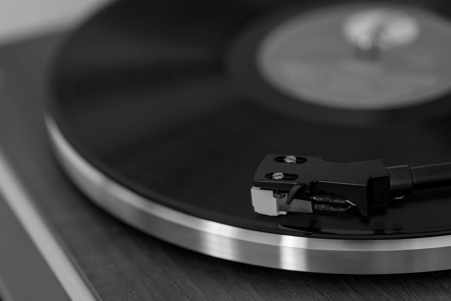 Close-up black and white shot of a vinyl record turntable tonearm and platter in dramatic lighting.