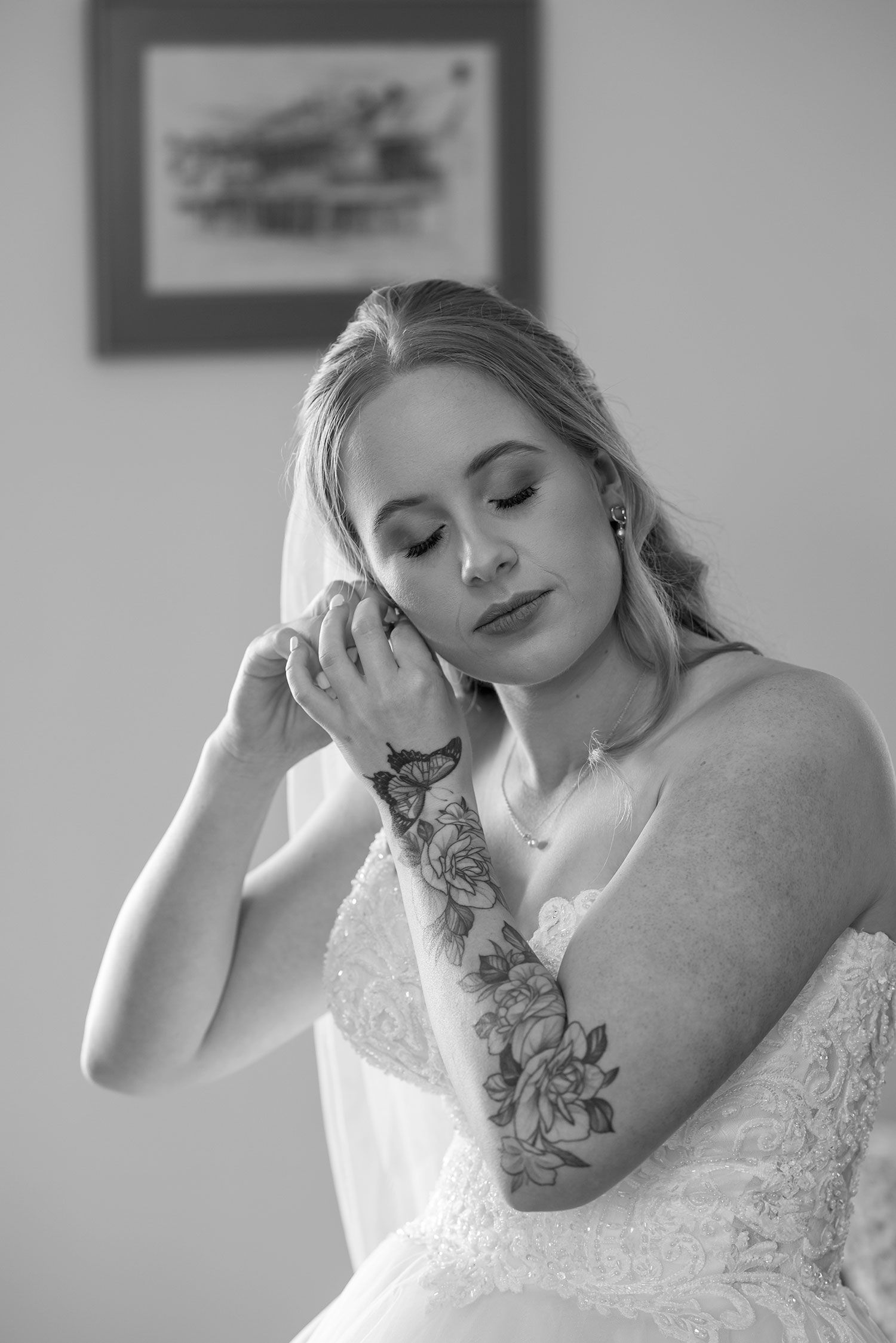 Black and white portrait of a Bride with floral arm tattoo wearing a white dress in a serene posed moment.