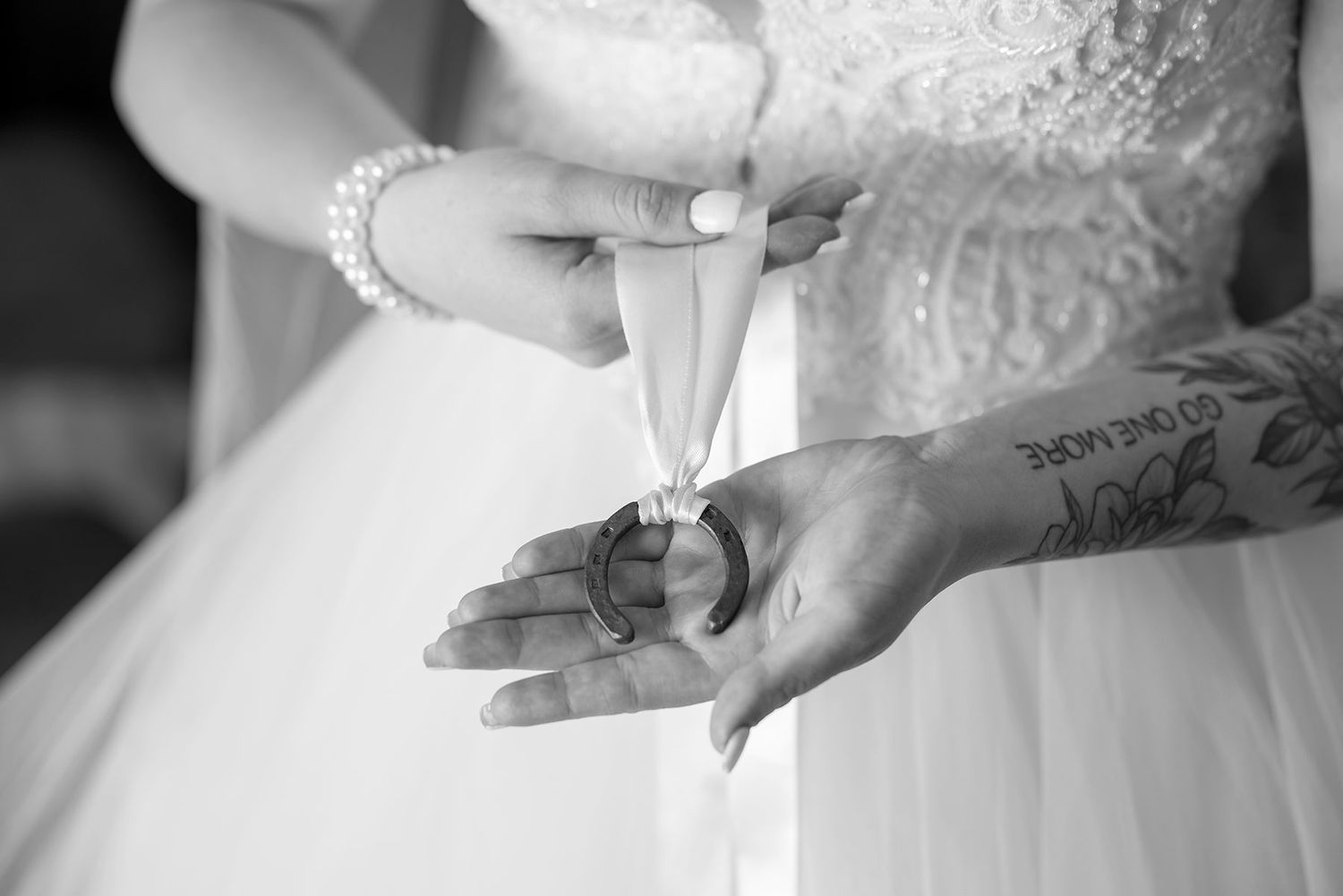 Black and white shot of hands with tattoos holding a Good Luck Horse Shoe during a wedding ceremony.