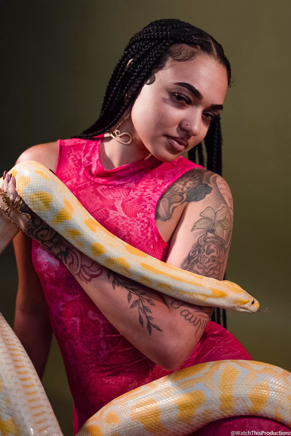 Model in pink lace dress poses with albino snake in artistic photoshoot against dark background.