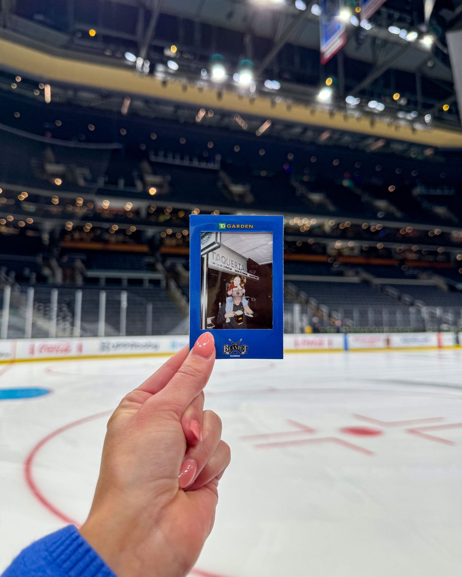 A vintage hockey trading card held up in front of an empty professional ice hockey rink with arena seating visible.