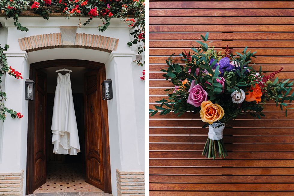 A white wedding dress hangs in a doorway with floral accents next to a colorful multi-rose bridal bouquet on wood background.