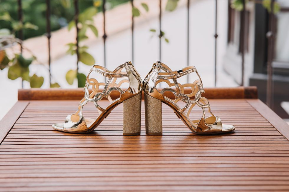 A pair of gold strappy heeled sandals with chunky block heels on a wooden deck or table outdoors.