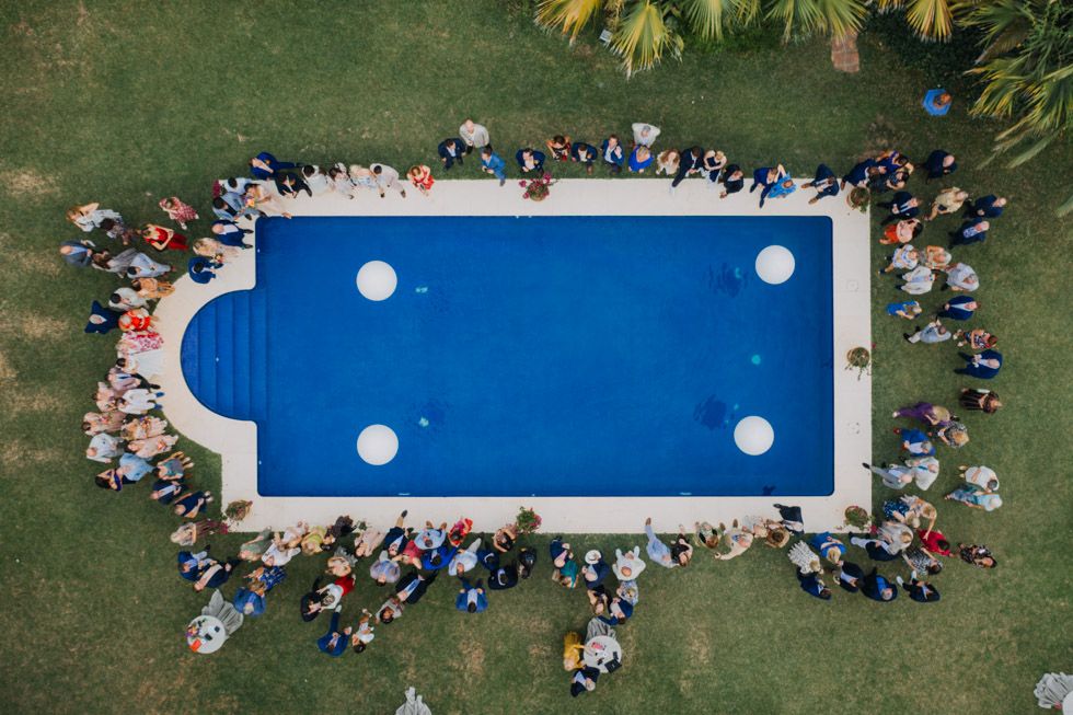 Aerial view of crowd gathering around rectangular blue swimming pool on grass lawn.