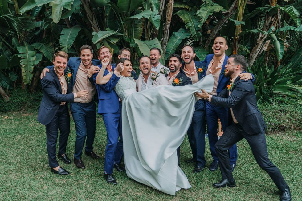 A playful wedding party poses together in a tropical garden setting with dramatic flair.