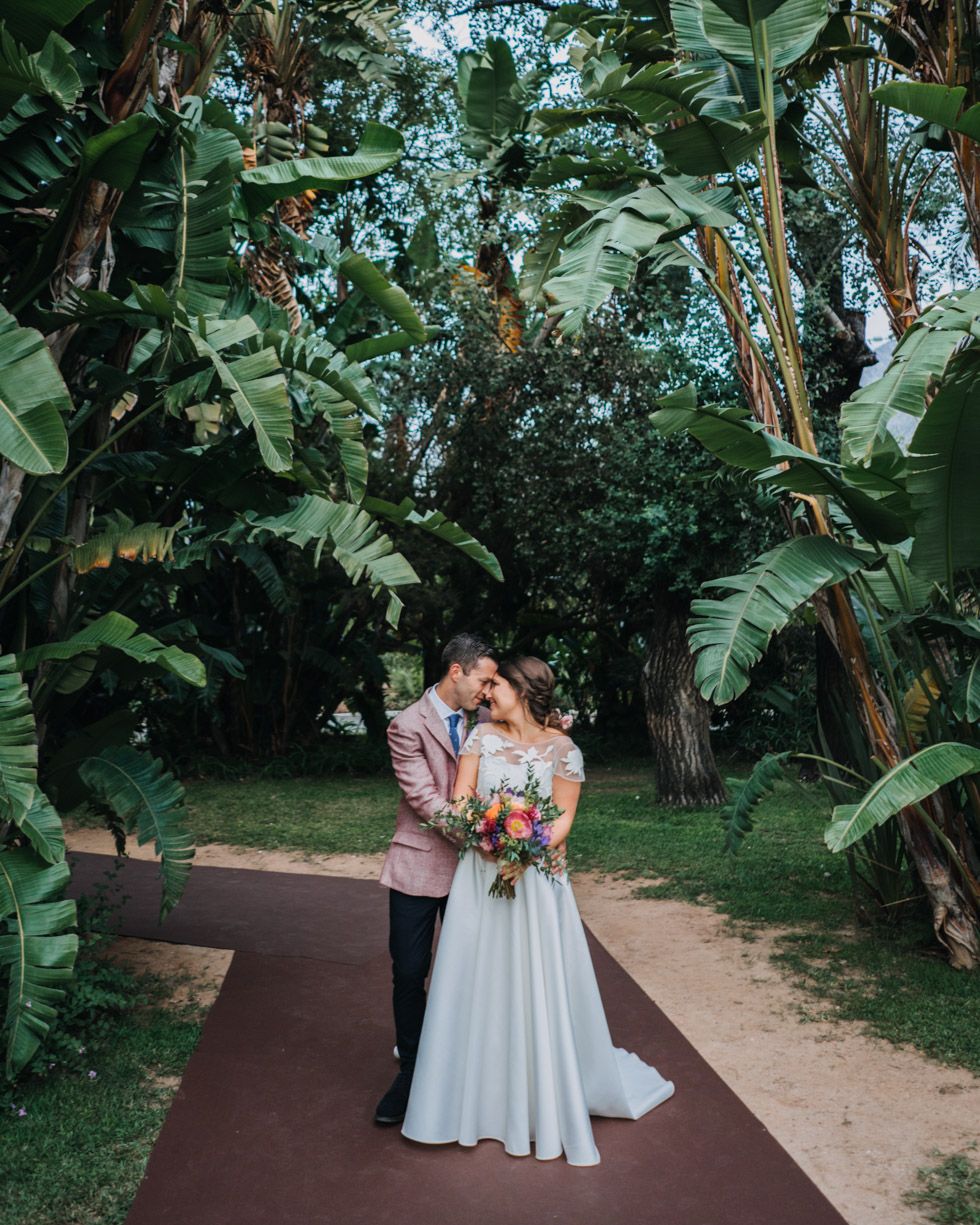 A couple embraces on a garden path surrounded by lush tropical banana leaf plants and greenery.