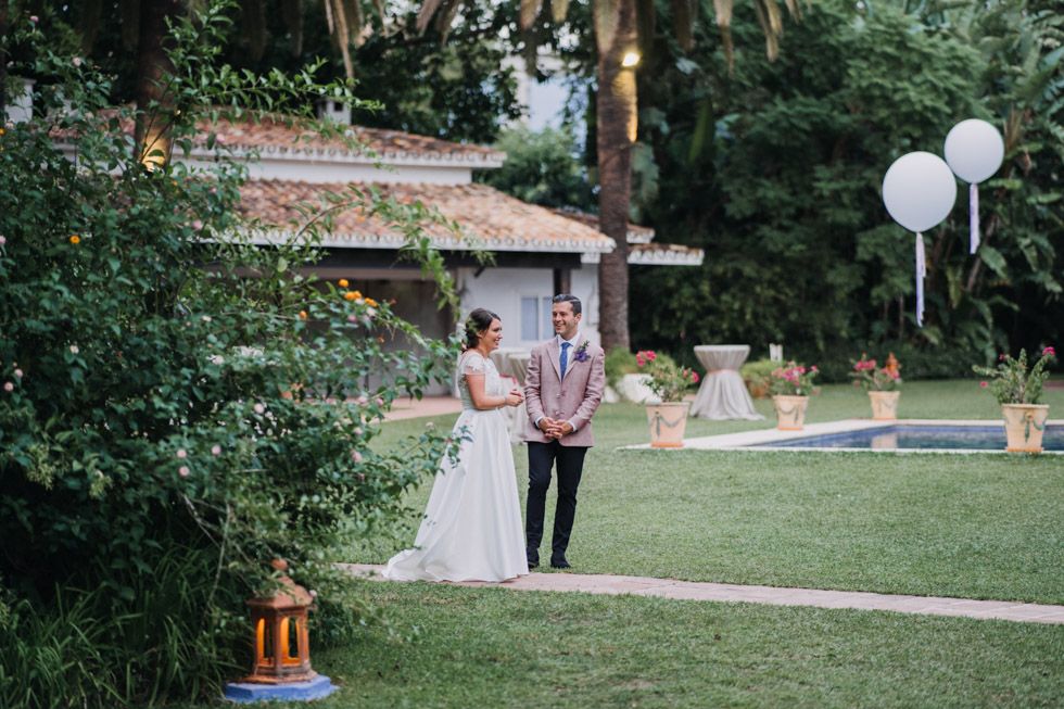 A couple stands together on a lush garden lawn decorated with white balloons and lanterns for an outdoor celebration.