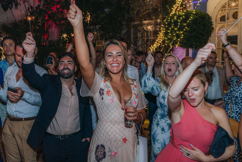 A lively celebration scene with dancing guests under twinkling lights at an evening outdoor party.