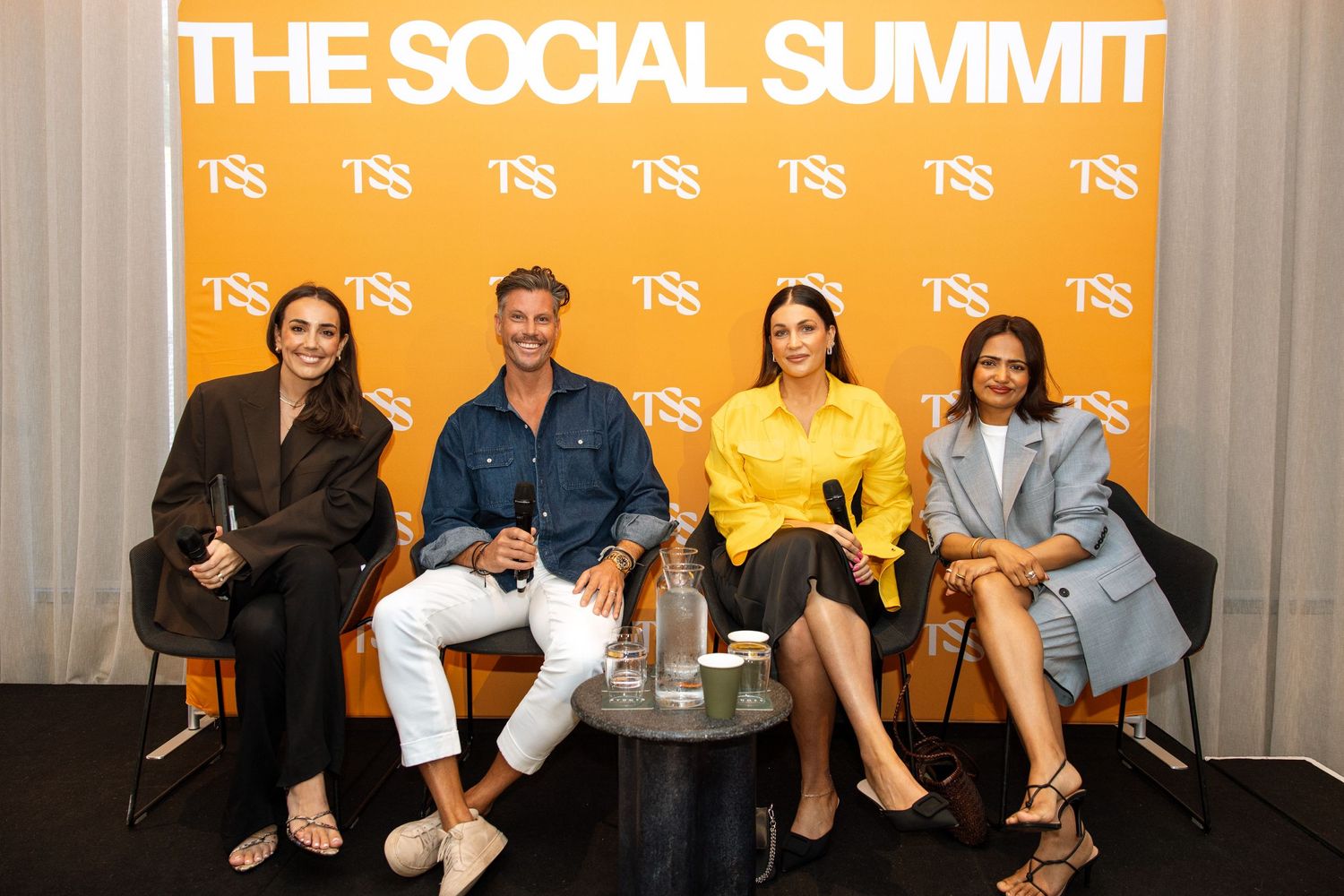 Four people seated on a panel at The Social Summit conference event with orange backdrop.