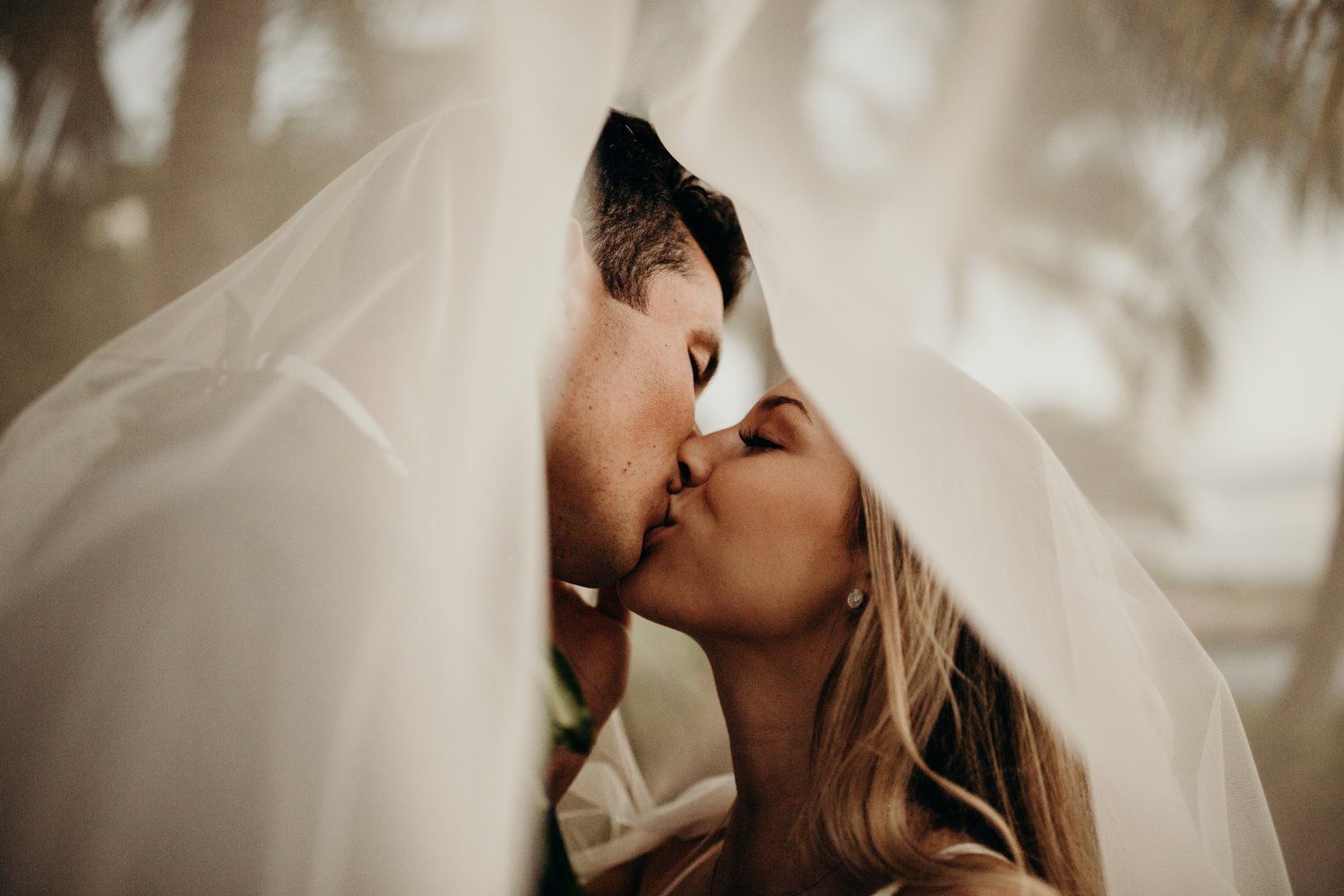 A romantic moment captured under a white veil with soft, dreamy lighting.