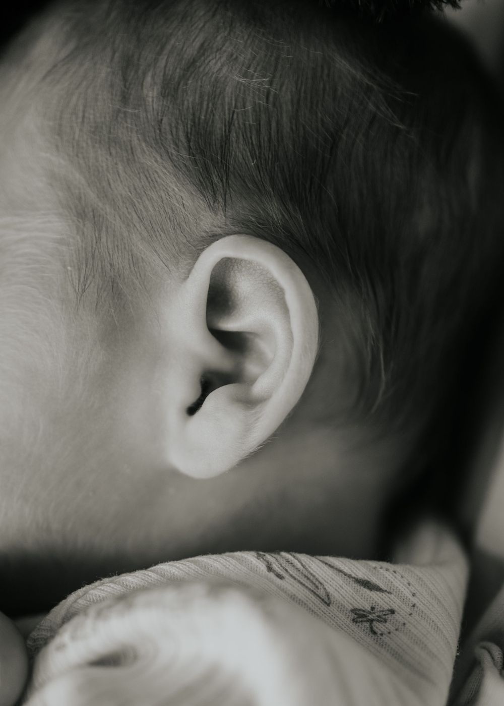 Close-up black and white photo of a tiny ear with soft baby hair captured during a newborn session at home in Farmington Minnesota