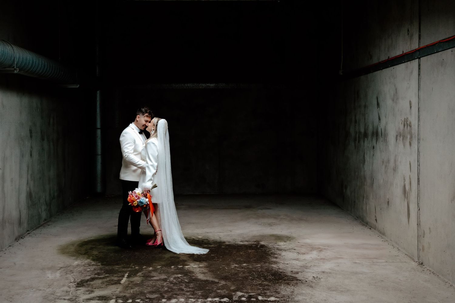 A romantic wedding moment with a flowing veil in a dark industrial setting.