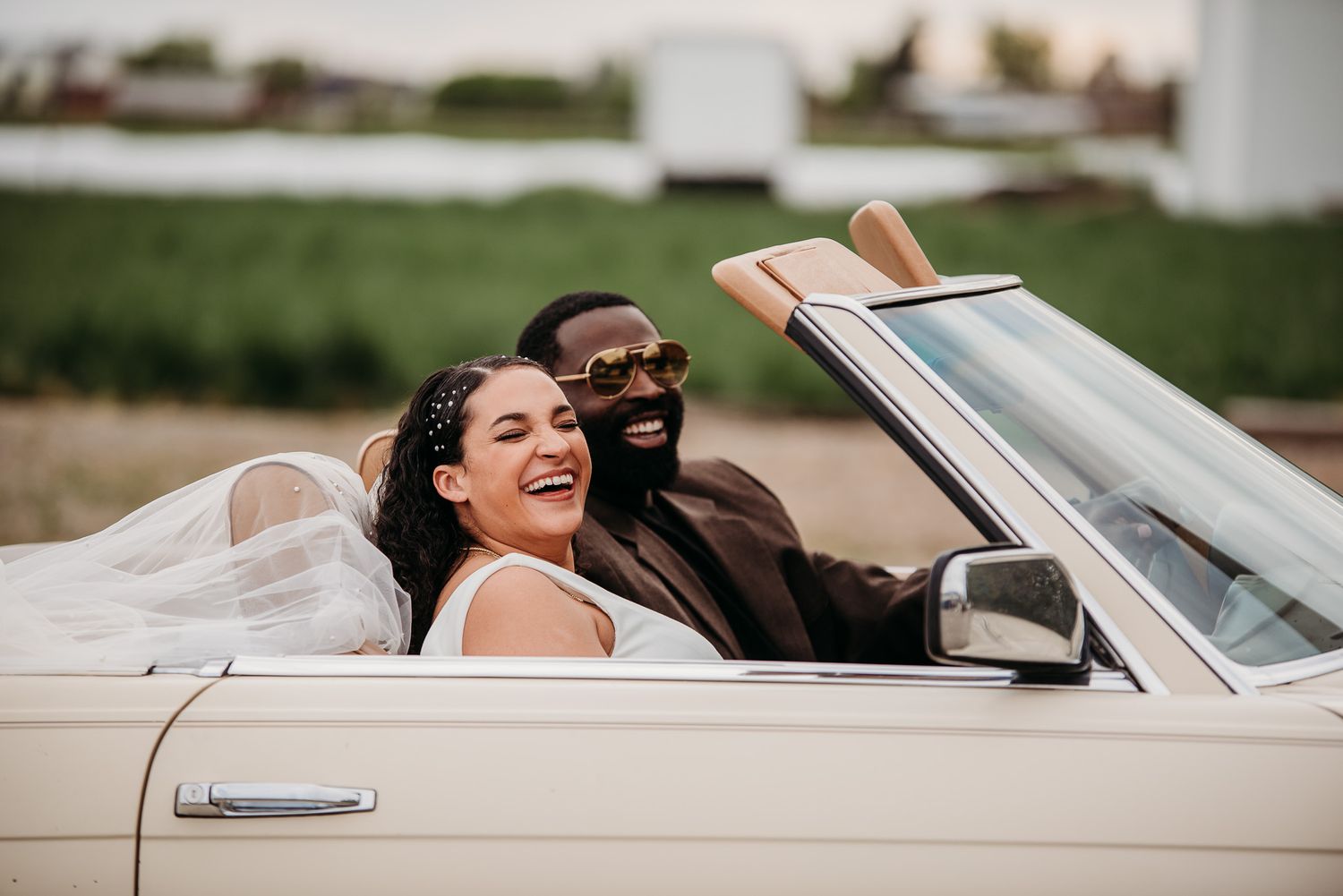 Joyful couple riding in vintage convertible car while celebrating their wedding day.