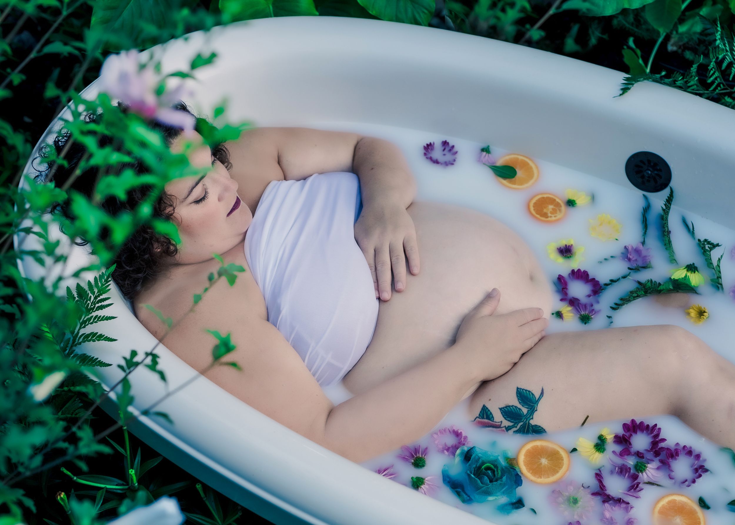 Maternity photoshoot in milk bath with flowers surrounded by tall bushes, outdoor maternity session in Windsor captured by Tasha Cannaday.