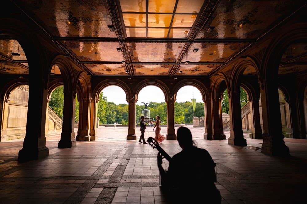 Historic covered colonnade with arched stone columns casting dramatic shadows in warm evening light at Bethesda Terrace.