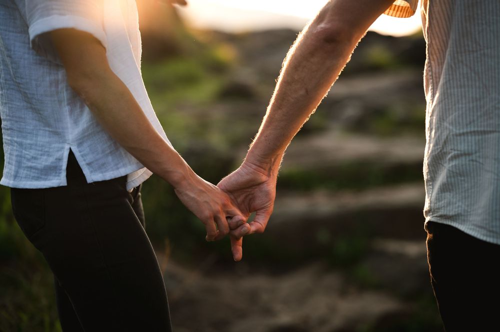Close-up shot of hands holding each other against a sunset sky and natural outdoor background.