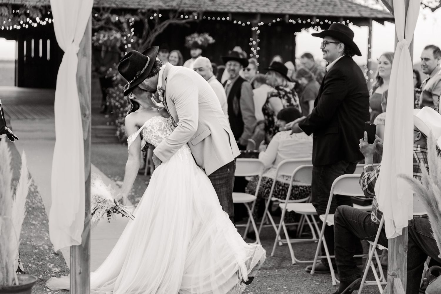 Black and white photo of wedding guests dancing and celebrating at an outdoor reception.