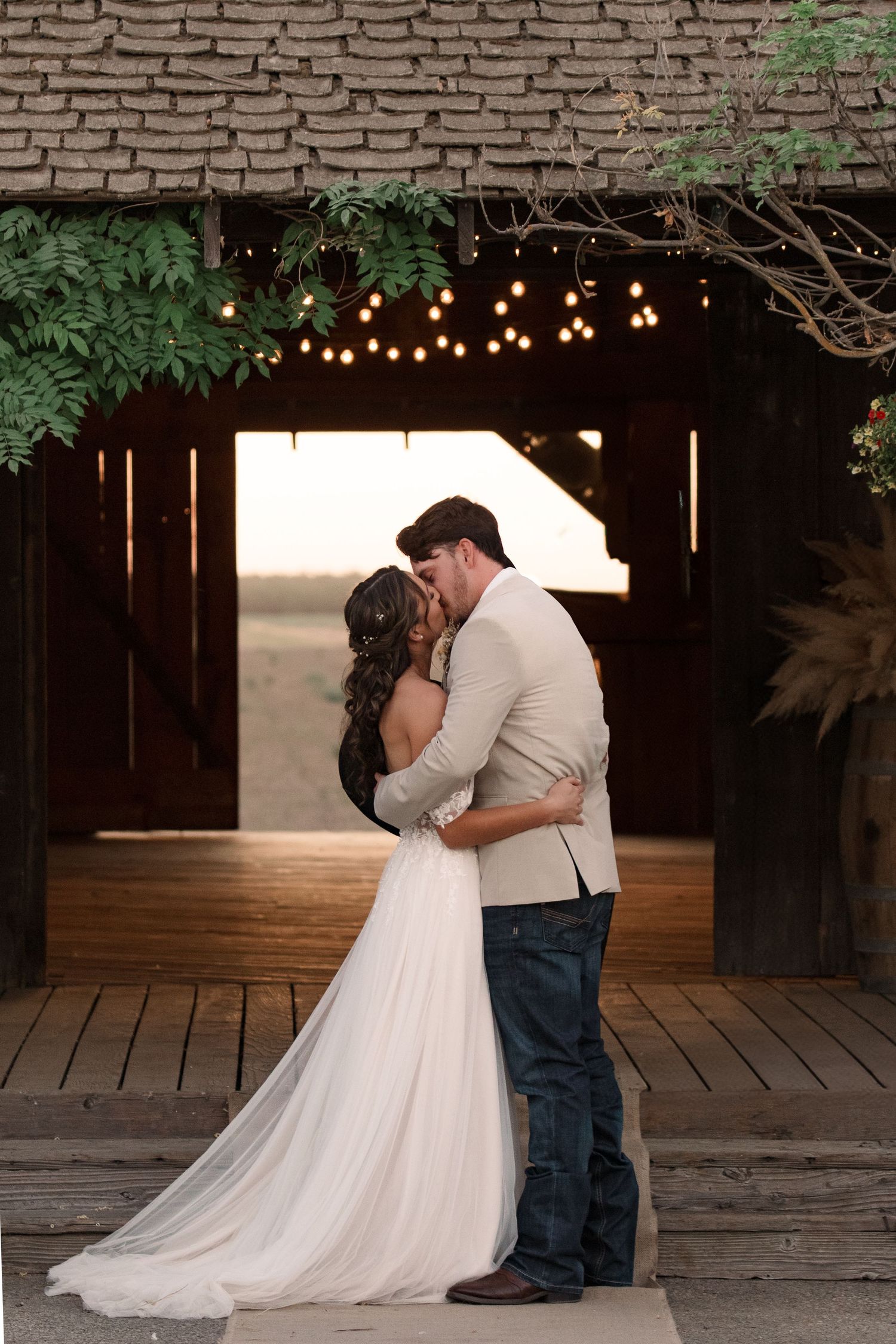 Intimate wedding photos taken under twinkling lights in a rustic barn setting.