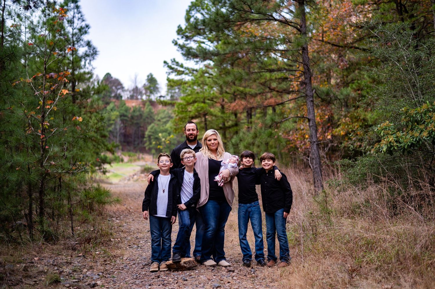 Blonde mother and father posing with four sons on wooded trail in fall.