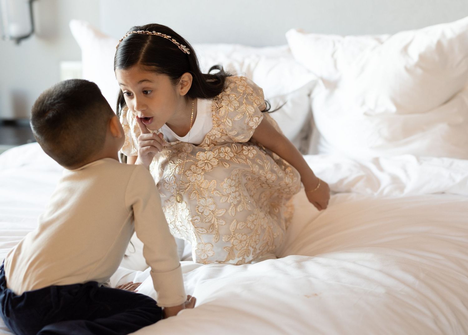 Two people share a tender moment on white bedding wearing formal attire.