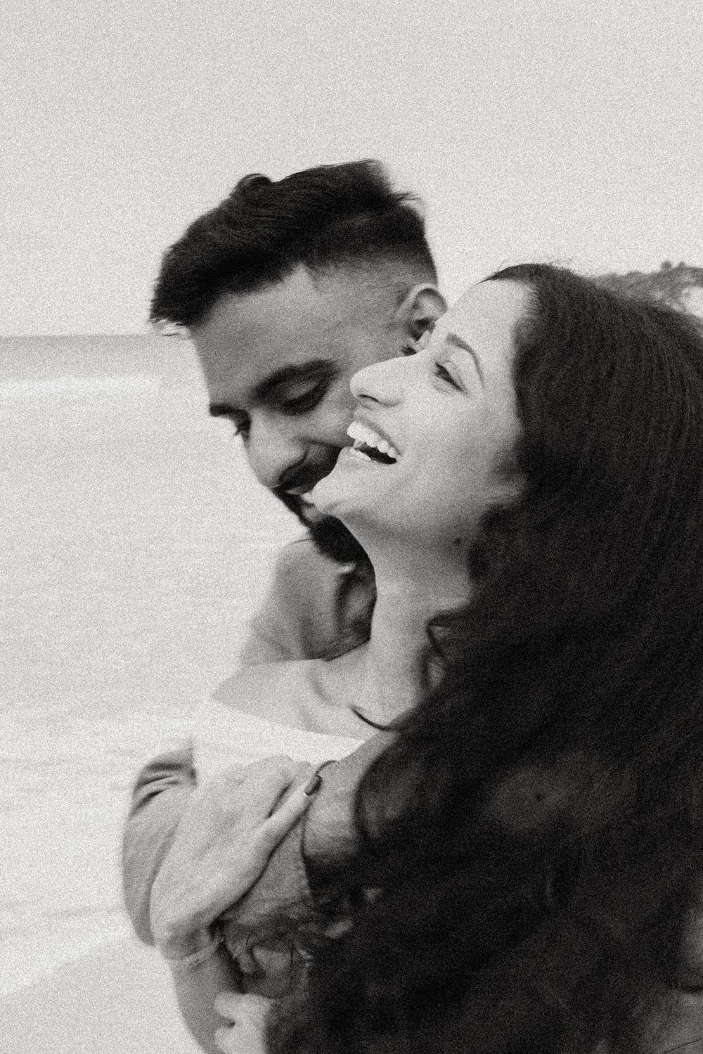 A black and white close-up captures a shared moment of laughter at the beach.