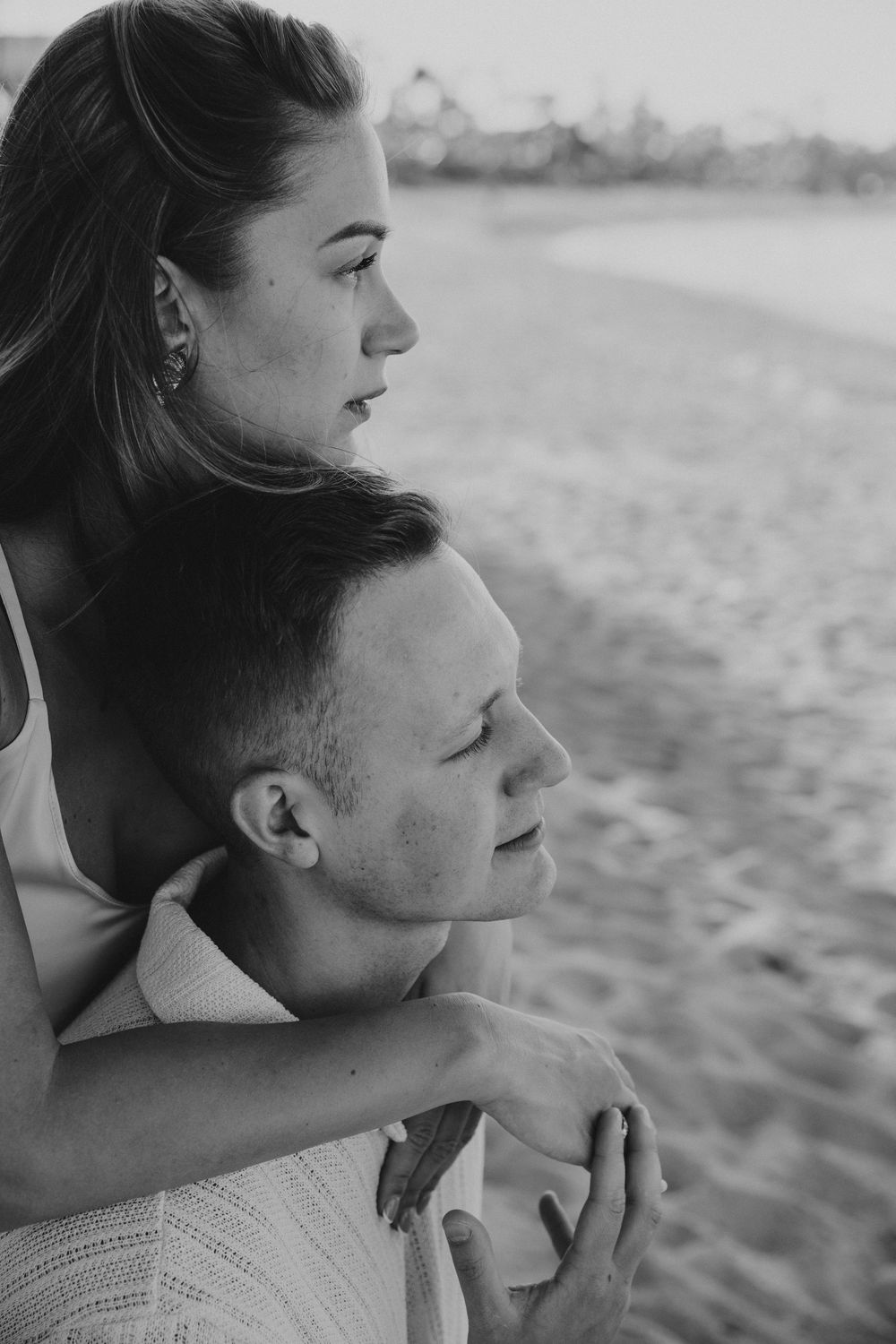 A black and white intimate portrait captures a tender beachside embrace.