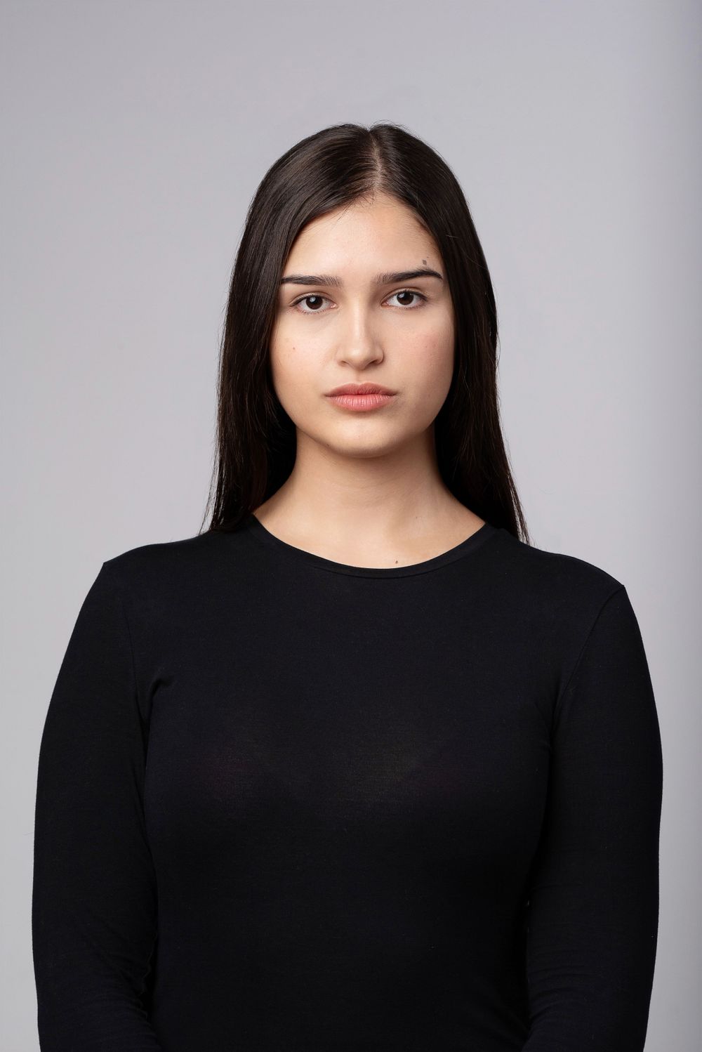 Portrait photo of someone with long dark hair wearing a black long sleeve top against a gray background.