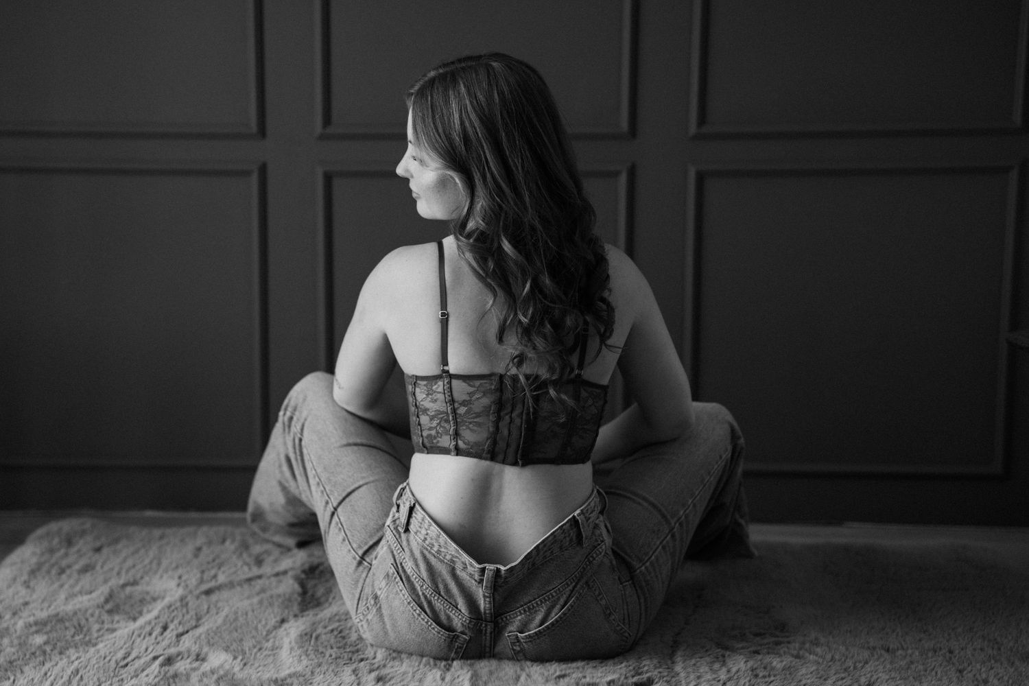 Stilvolles Schwarz-Weiß-Boudoir-Porträt einer Frau in Spitzen-Lingerie und Jeans.