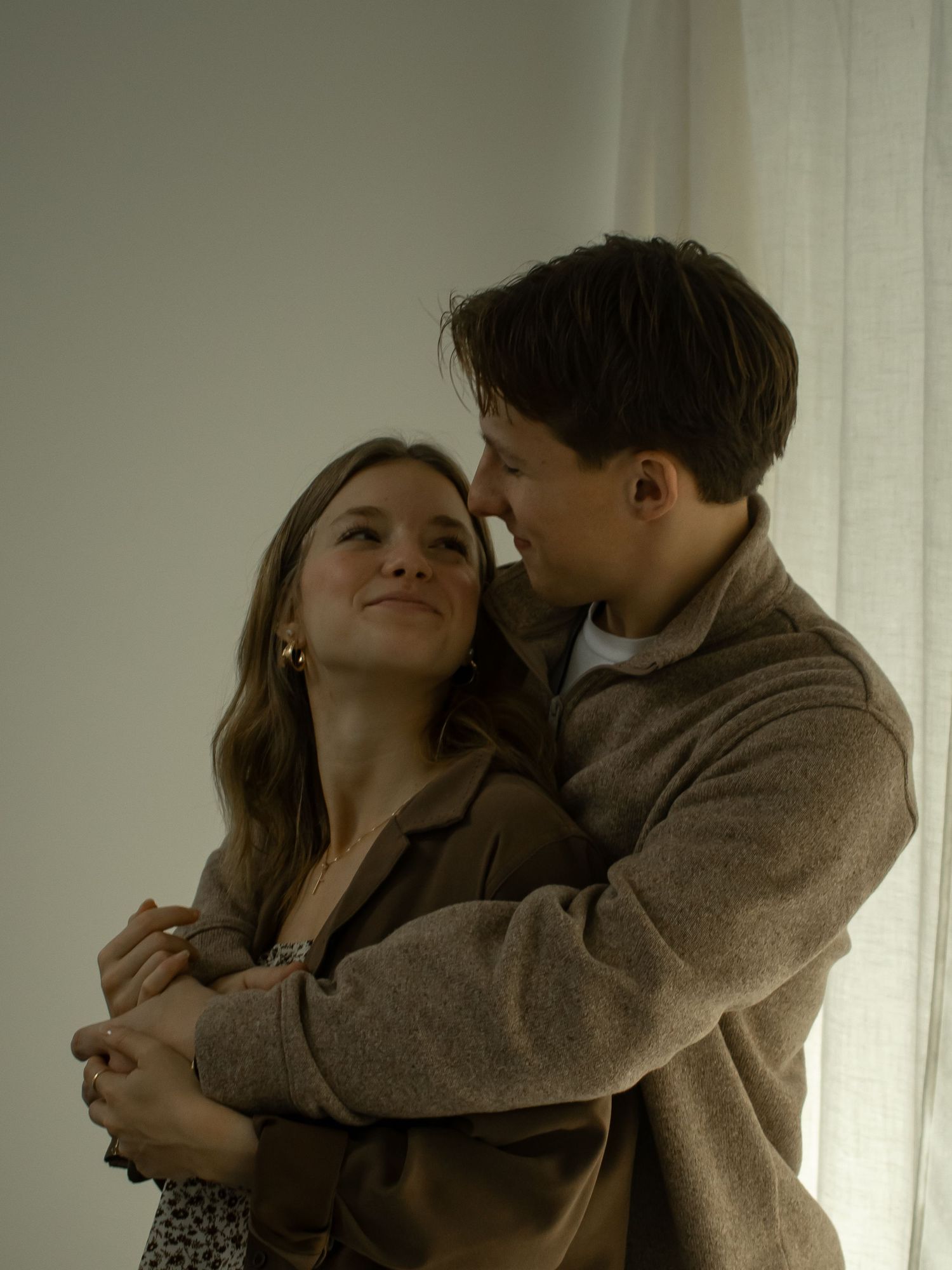 Intimate couple embracing by window in cozy sweater and casual attire.