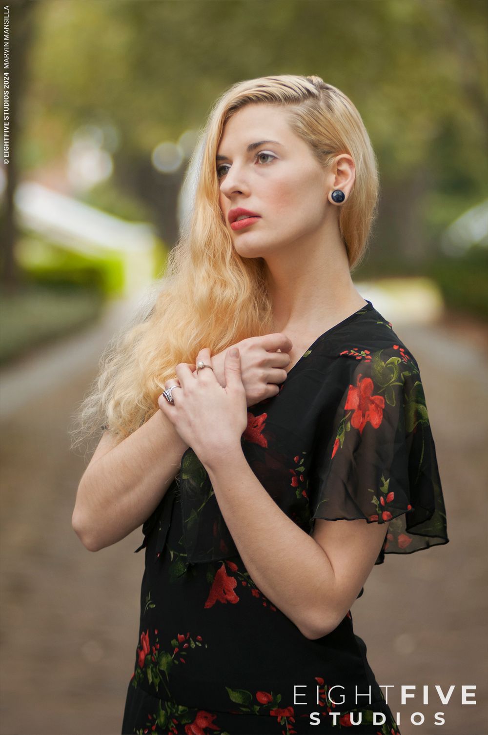 Blonde woman in black floral dress with red flowers posing outdoors by Eight Five Studios.