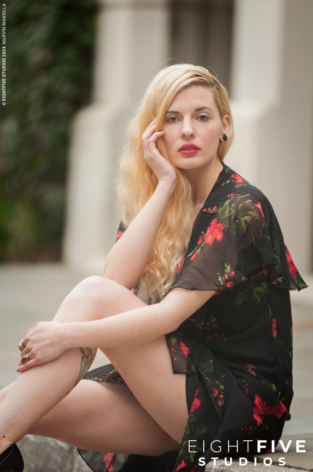 Blonde woman in black floral dress sitting on steps posing by Eight Five Studios.