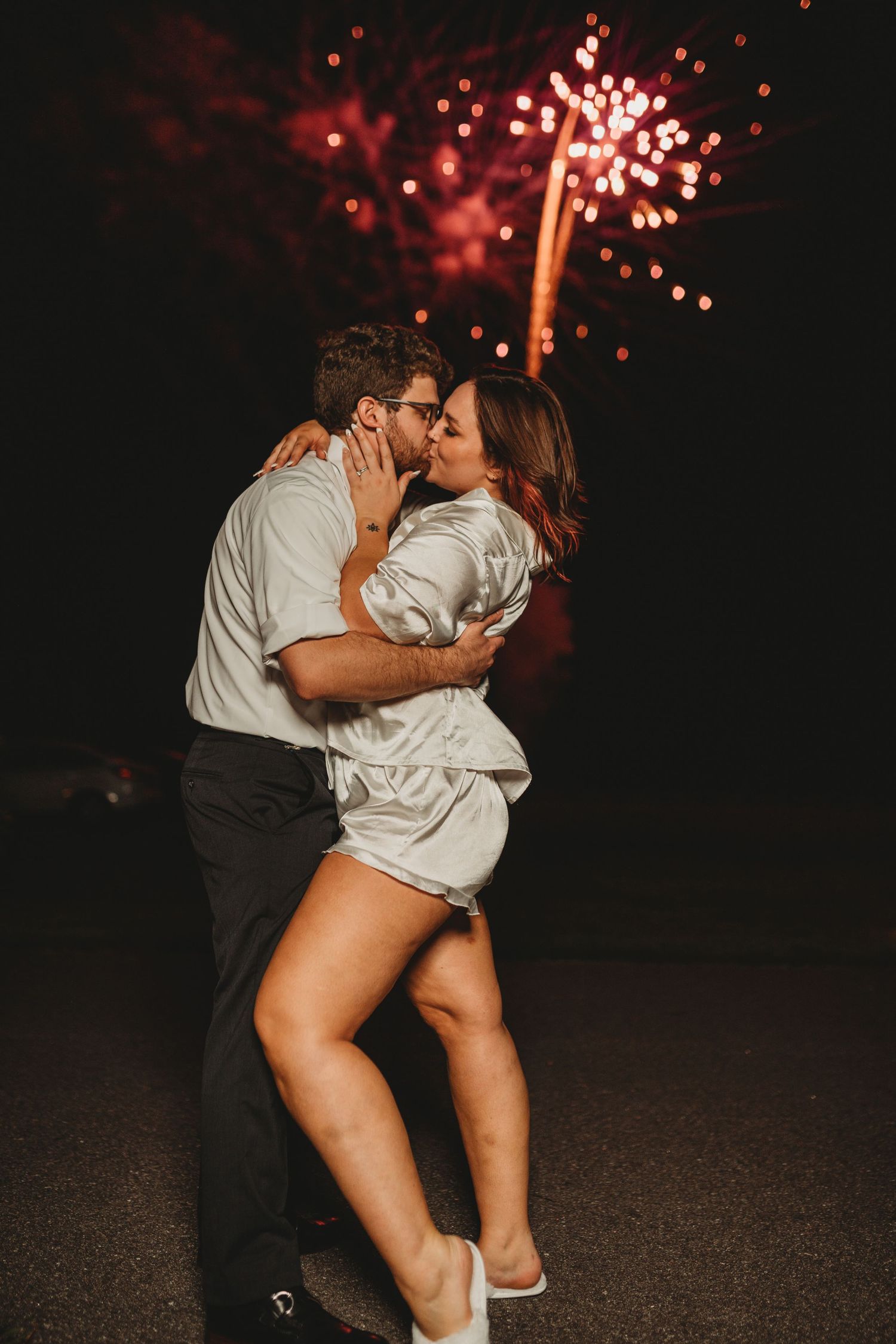 Romantic couple embraces under red fireworks display during nighttime celebration.