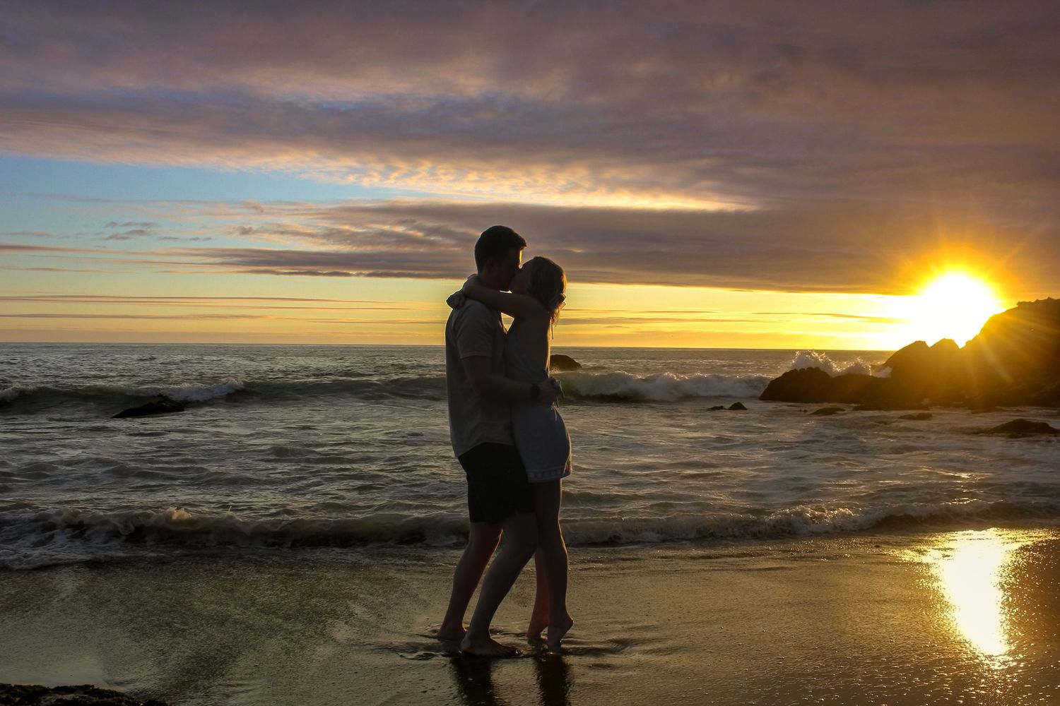 A couple embracing in a kiss on a Laguna Beach at sunset. A proposal engagement photoshoot photographer Noony Photography Co.