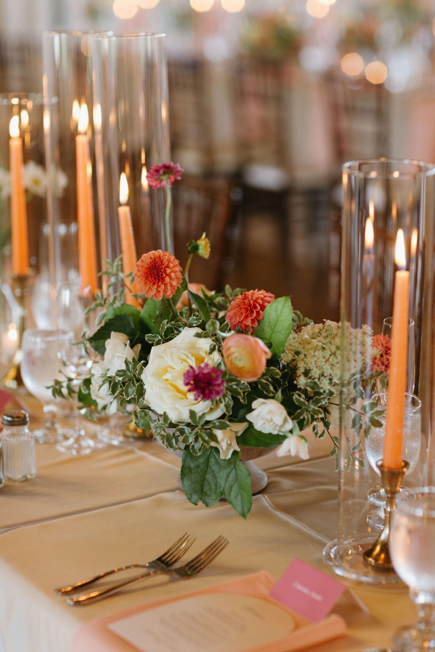A romantic table setting with tall taper candles and colorful floral centerpiece featuring coral dahlias.