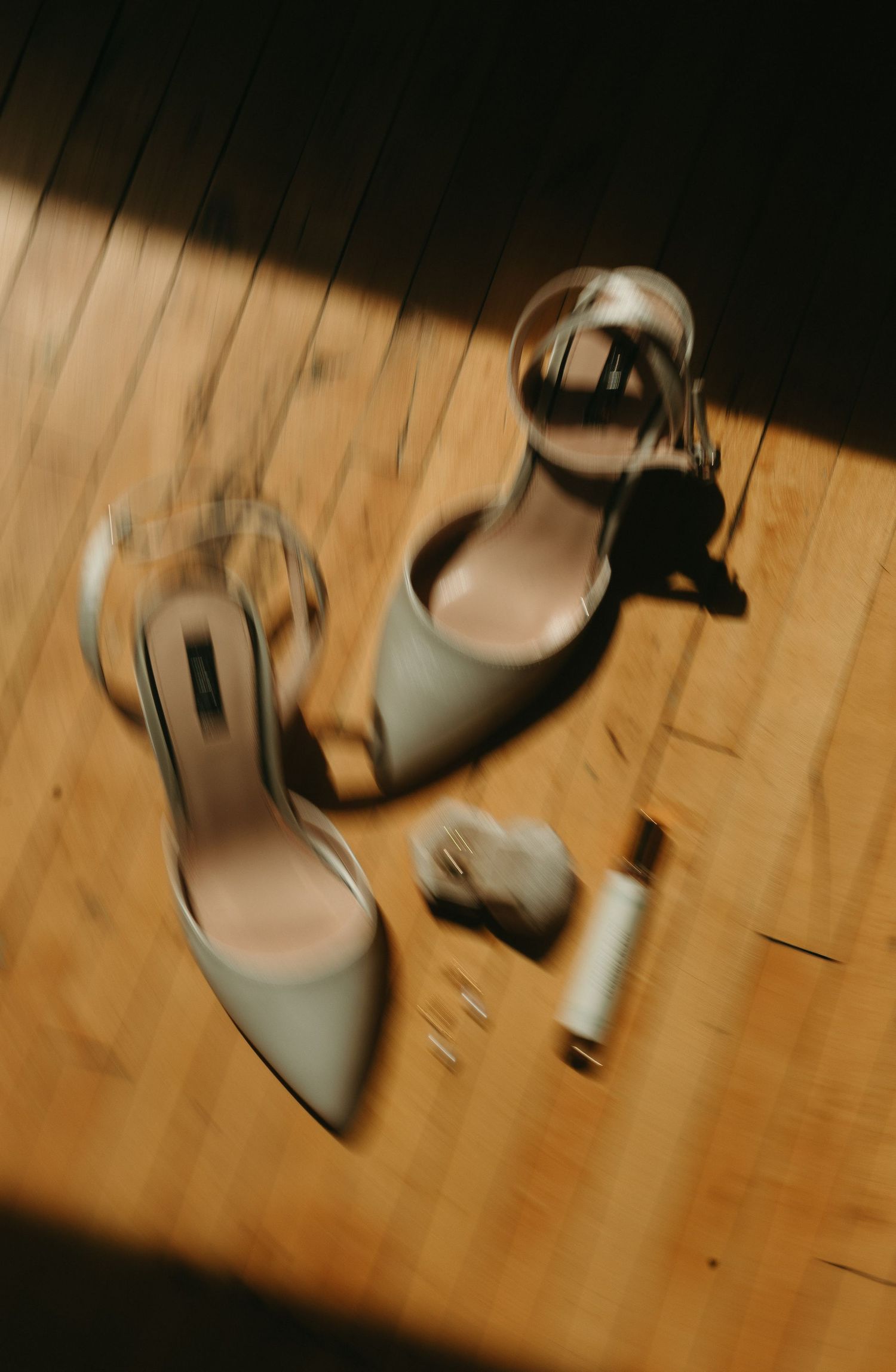 Elegant white bridal heels on a hardwood floor with dramatic lighting and shadows.