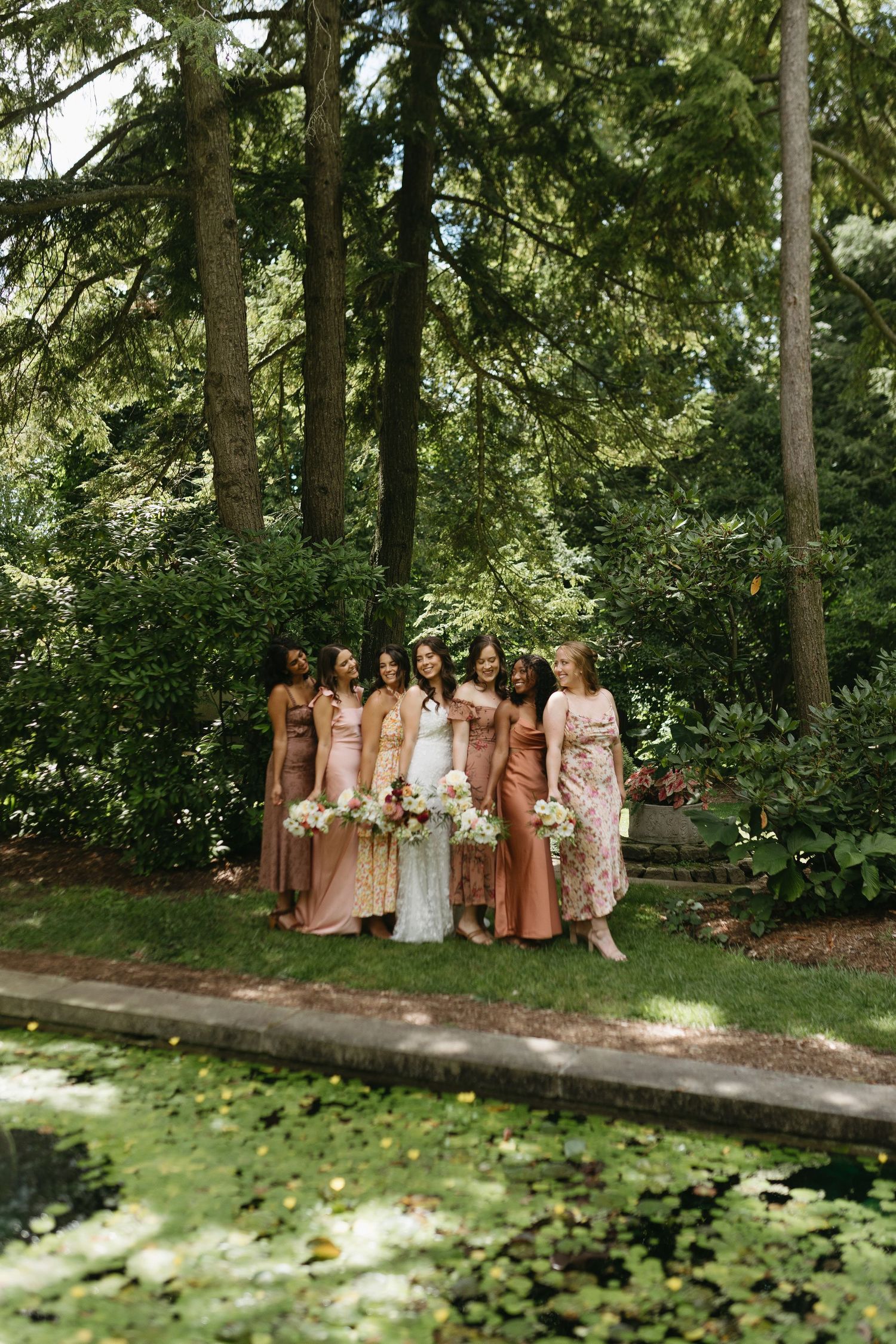 Wedding party in blush and neutral tones posed together in a garden setting.