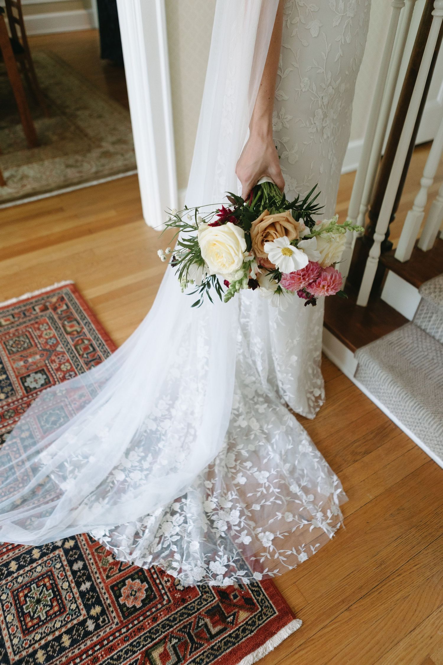 Detail shot of a lace wedding dress train with delicate floral embellishments on hardwood floor.