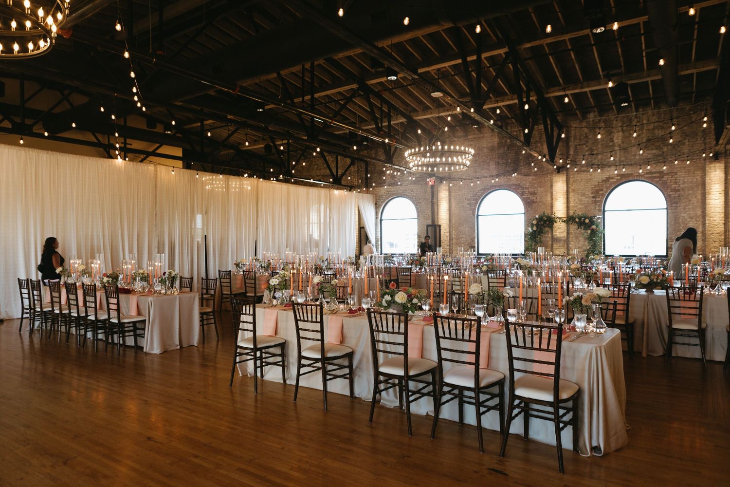 Spacious wedding reception venue with white draping, elegant table settings, and warm lighting.