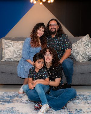 Family of four posing together in living room, wearing coordinating outfits with blue and black patterns.