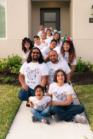 Large extended family in matching white shirts posing on outdoor steps in front of home.
