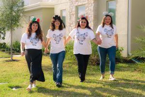 Four women in matching white Disney shirts walking hand-in-hand on green lawn.