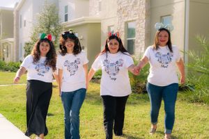 Four women wearing matching white Disney shirts and colorful mouse ears walking outdoors.
