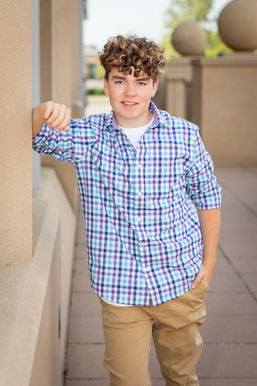 Portrait session along covered walkway wearing checkered shirt and khaki pants.