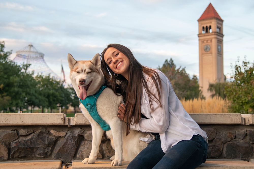 Young woman hugging a husky dog outdoors with Spokane clock tower visible in the background.