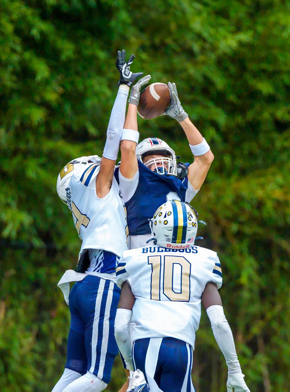 Football players leap to catch the ball during a competitive play with a green background.