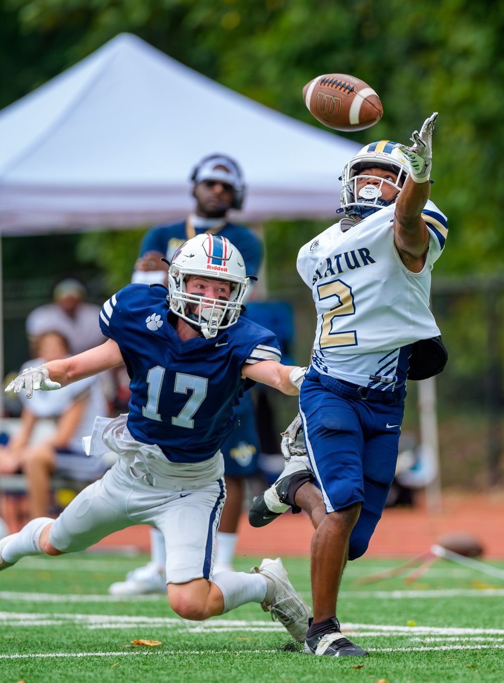 Two players compete for a football pass with one diving and another reaching for the catch.