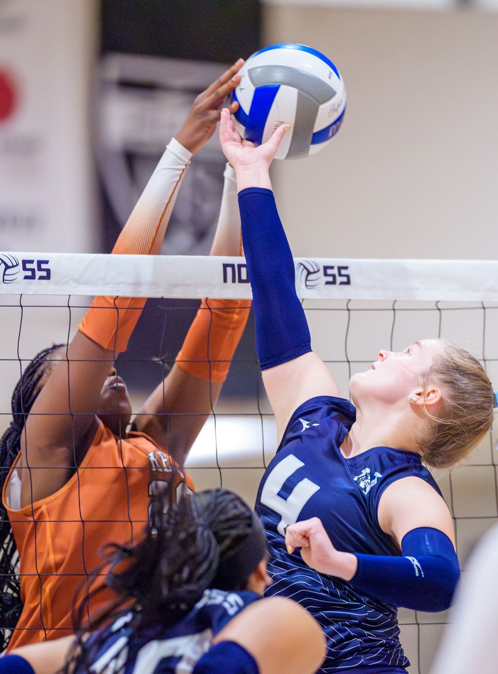 Two volleyball players battle at the net for control of the ball during an intense play.